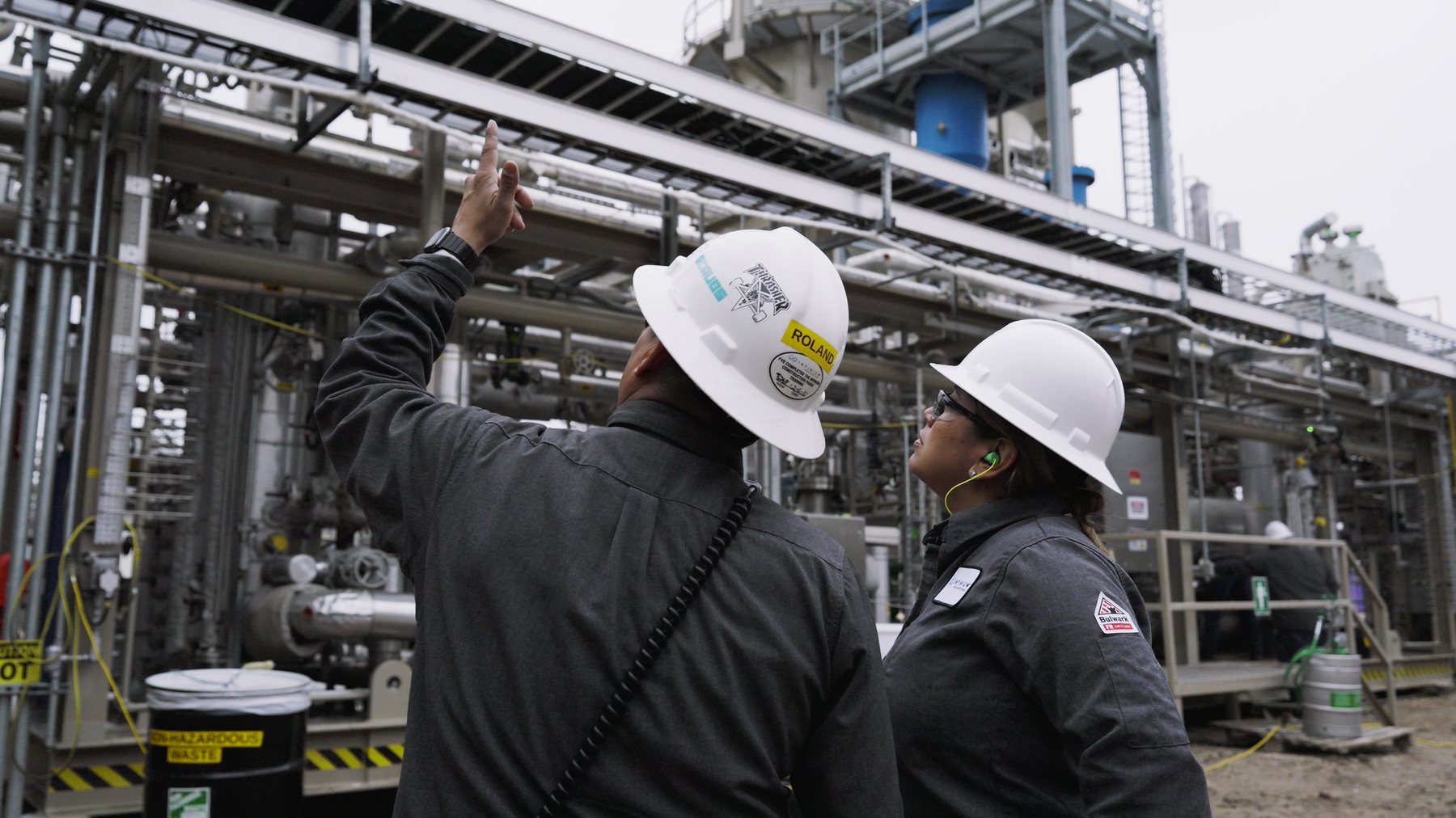 Two Infinium operators in flame-resistant clothing and hard hats looking up at the Pathfinder process structure